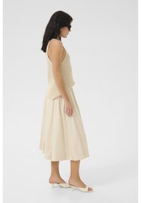Top in maglia beige abbinato a una gonna midi beige e mule con tacco a blocco beige, visto di lato su uno sfondo semplice.