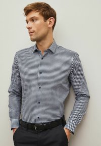 Cămașă cu model vichy în albastru închis și alb, cu mâneci lungi, design cu nasturi, dotată cu guler. Purtați cu o curea neagră și pantaloni închiși la culoare.