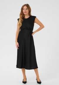 Musta midi-mekko, jossa on lyhyet hihat ja solmittu yksityiskohta vyötäröllä. Sujuva kangas, virtaava hame, jossa on hieno kiilto.
