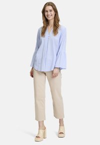 Hellblau-weiß gestreifte Bluse mit Glockenärmeln, V-Ausschnitt und Knopfdetails, kombiniert mit beigen, cropped Hosen und cremefarbenen Blockabsatzschuhen.
