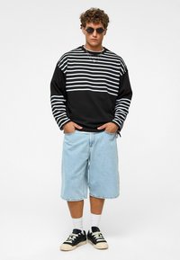 Zwart-wit gestreepte sweatshirt, lichtblauwe denimshorts en zwarte sneakers met witte accenten, gecombineerd met ronde zonnebrillen.