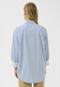 Chemise à rayures bleu clair avec une coupe décontractée, manches longues, col standard et poignets blancs contrastés.