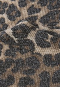 Stickad tyg i beige och brunt med ett leopardsmönster i mörkgrått. Texturerad yta med synliga fibrer och oregelbundna former.