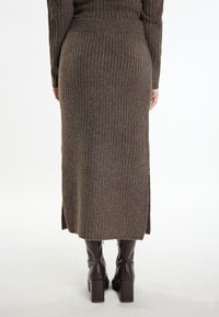 Jupe midi en tricot côtelé marron avec une fente sur le côté, taille cintrée et tissu texturé. Associée à des bottes brunes à talons montantes.