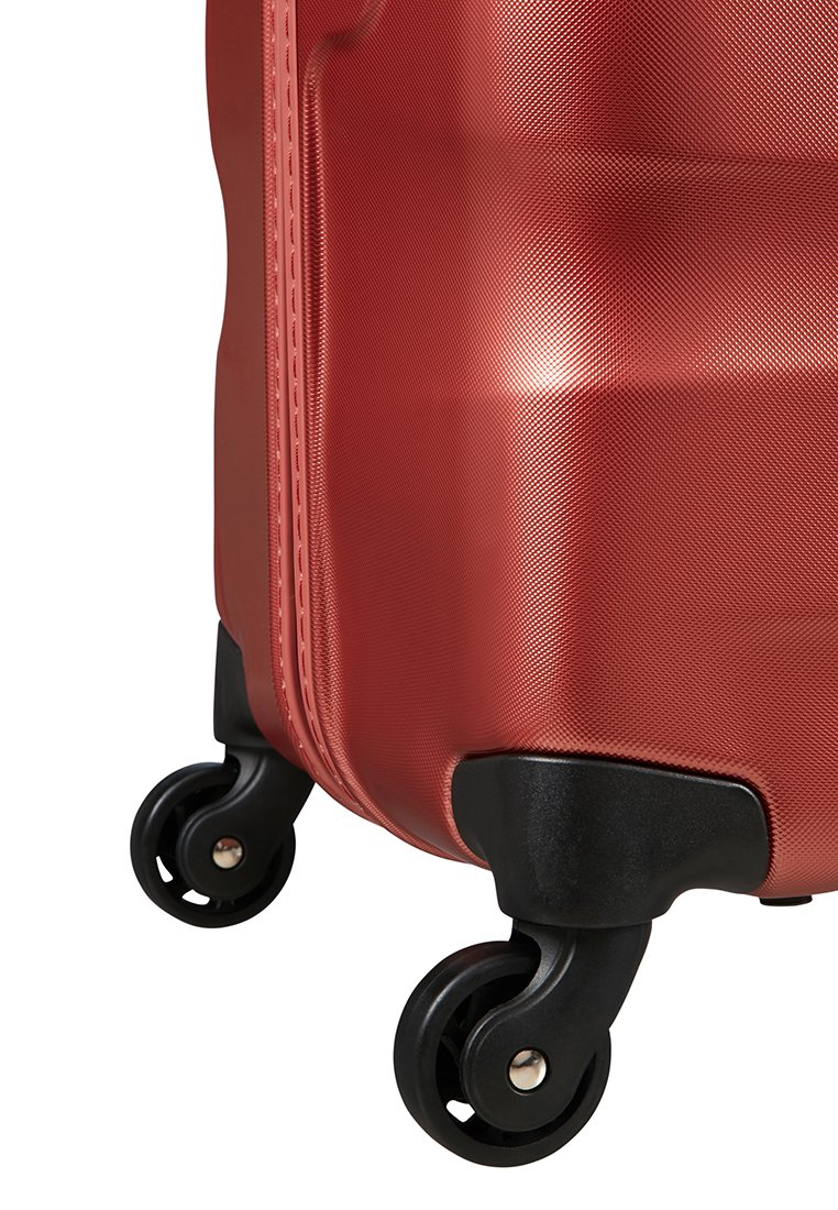 Maleta roja de hard-shell con superficie texturizada, que cuenta con ruedas y acentos negros. El cuerpo tiene un diseño curvado con bordes reforzados.