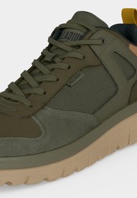 Baskets vert olive avec panneaux en daim et mesh mélangés, lacets assortis, semelle beige et languette jaune au talon, marquage Palladium sur la languette et le côté.
