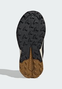 Semelle de chaussure de trail avec une base en caoutchouc noir, présentant un motif texturé et des crampons de traction proéminents ; accent en caoutchouc marron à l'arrière.