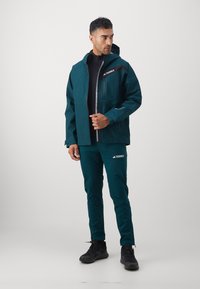 Waterproof teal jacket with a zippered chest pocket and adjustable hood, paired with matching pants. Durable, breathable fabric.
