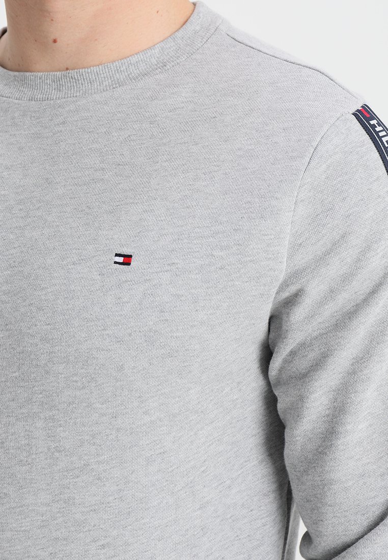 Sweat-shirt en coton gris avec un col rond, présentant un petit logo brodé en rouge, blanc et bleu sur la poitrine et un détail de logo sur la manches.