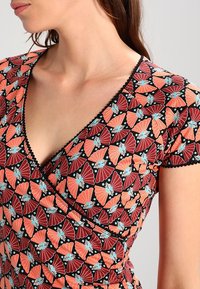 Zavinovací šaty s živým vzorem motýlích křídel v červené, oranžové a modré barvě na černém pozadí; krátké rukávy a vykrojené lemování.