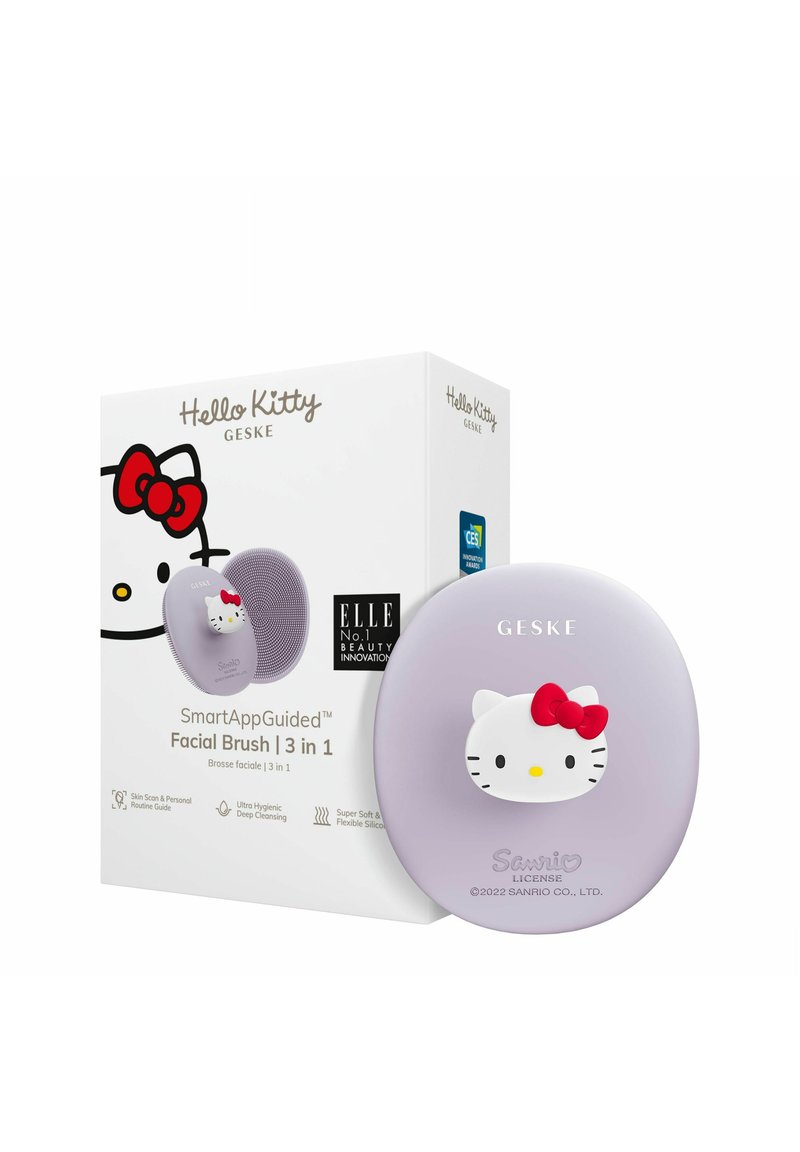 Hello Kitty ansiktsborste i ljuslila silikon med ett upphöjt vitt katt-design som har en röd rosett. Lådan inkluderar produktinformation och logotyper.