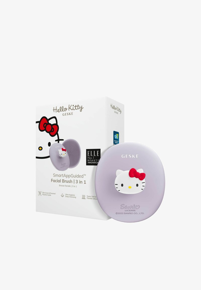 Hello Kitty ansiktsborste i ljuslila silikon med ett upphöjt vitt katt-design som har en röd rosett. Lådan inkluderar produktinformation och logotyper.
