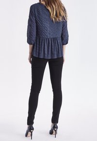 Námořnická modrá plisovaná blůza s tříčtvrtečními rukávy a rozšířeným lemem, v kombinaci s černými skinny džíny a černými stiletto podpatky.