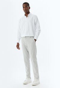 Camisa blanca de botones con mangas largas, combinada con pantalones ajustados de color gris claro y zapatillas blancas. Diseño y ajuste simples y limpios.