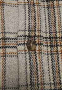 Tissu à carreaux avec des tons gris, beige et orange, présentant un tissage texturé. Un bouton rond et translucide est bien en vue.