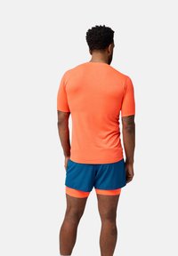 Ropa deportiva para hombres: camiseta ajustada de manga corta naranja, pantalones cortos azules con acentos naranjas. El material parece ligero, adecuado para actividades atléticas.