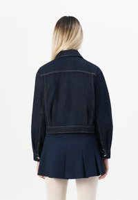 Mørkeblå denimjakke med cropped design, knappemanchetter og klassisk krage. Bakken har sydd detaljer og en ren finish.