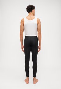 Black leggings with a slim fit and textured fabric, featuring an elastic waistband. Worn with a white tank top, model standing barefoot.