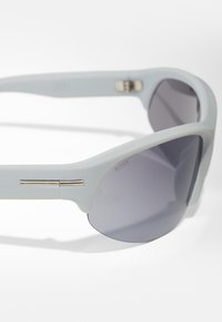 Gafas de sol azul claro con lentes gris ahumado. Presentan una montura elegante, detalles plateados en las patillas y un acabado mate.