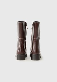 Bottines en cuir marron avec un léger talon, dotées d'une fermeture éclair à l'arrière, présentées sur un fond clair uni.
