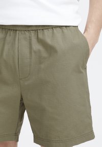 Texturált anyagból készült khaki rövidnadrág, rugalmas derékkal, oldalsó zsebekkel és egyenes szabással, finom rácsos mintával.