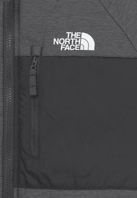 Šedá bunda s hladkou texturou, temným panelem a bílým logem "The North Face". Součástí je také detail kapsy na zip.