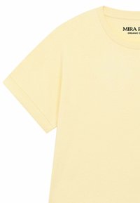 T-shirt jaune clair en coton biologique à manches courtes, col rond et étiquette de marque "MIRA" visible à l'intérieur du col.