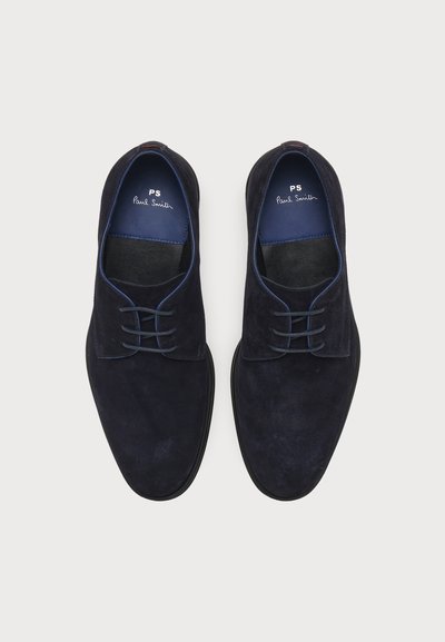 Paire de chaussures habillées en daim noir à lacets avec des semelles intérieures bleues étiquetées PS Paul Smith sur un fond clair uni.