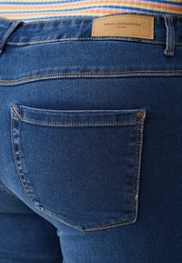 Dark blue denim jeans featuring a back pocket with visible stitching. A tan leather label at the waistband displays brand details.