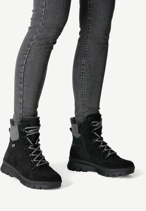 Botas negras hasta el tobillo hechas de gamuza y material sintético, con acentos grises y suelas gruesas y texturizadas. Son visibles los cordones y cremalleras.