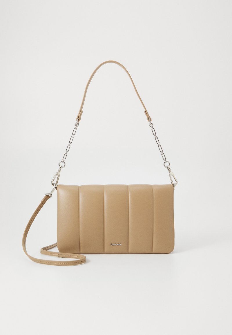 Sac à main rectangulaire beige avec rembourrage vertical, chaîne en argent et bandoulière en cuir, avec petit logo Calvin Klein à l'avant.