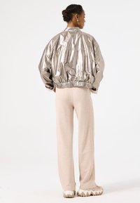 Metallic silver bomber jacket with elastic hem, paired with light beige pants. The design features a relaxed fit and smooth texture.