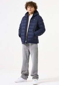Chaqueta de plumón marinera con capucha, con un diseño acolchado y cremallera en la parte delantera. Combinada con jeans gris claro y zapatillas blancas.