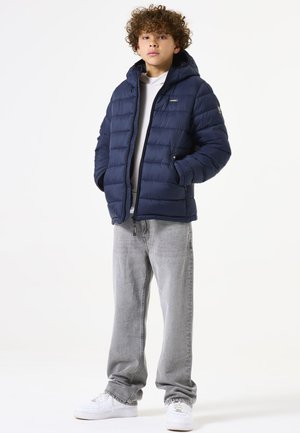 Chaqueta de plumón marinera con capucha, con un diseño acolchado y cremallera en la parte delantera. Combinada con jeans gris claro y zapatillas blancas.