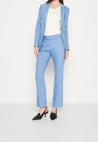 Světlomodrý oblek s přiléhavým sakem a rovnými kalhotami. V kombinaci s černými sandály na podpatku. Hladká tkanina s elegantním střihem.