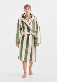 Gestreepte badjas in groen en lichtbeige. Gemaakt van zacht, fluwelig materiaal met een capuchon en een strikceintuur. Lange mouwen en een lengte tot aan de knie.