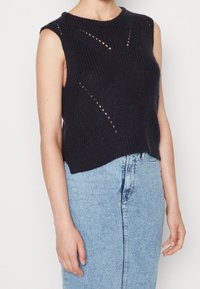 Marinblå ärmlös stickad topp med en texturerad design och utskärningar. Kombinerad med en ljusblå denimkjol som betonar den avslappnade stilen.