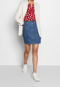 Jeanskjol, ljus tvätt, med rak skärning och framfickor. Matchas med en röd blus med vita cirklar och en vit kavaj.