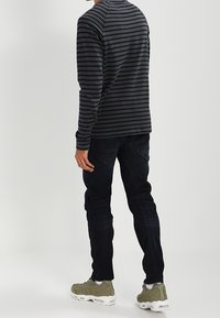 Chemise à manches longues, rayée gris foncé et noir, associée à un jean bleu foncé et des baskets vert olive. Design simple, silhouette cintrée.