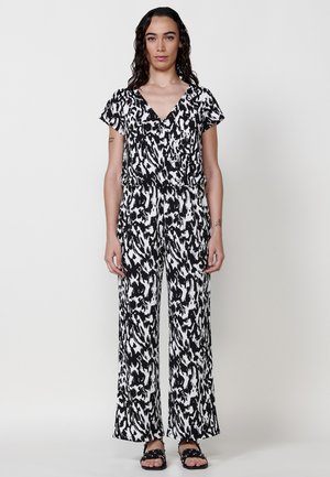 Combinaison à motifs noir et blanc avec un décolleté en V, des manches courtes, une taille élastique et des pantalons évasés. Paire de sandales noires avec des clous.
