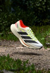 Leichter Laufschuh in Weiß mit schwarzen Streifen, roten Akzenten und gelben Schnürsenkeln; verfügt über ein strukturiertes Obermaterial und eine gepolsterte Sohle.