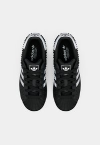 Baskets noires avec une tige texturée, trois bandes blanches, un bout en caoutchouc et une semelle rainurée. Présente un logo Adidas sur la languette.