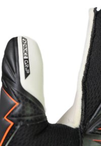 Gros plan sur le pouce d'un gant de gardien de but noir et blanc portant l'inscription "Advance Grip", avec un bord orange sur un matériau texturé.