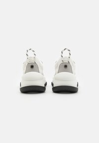 Scarpe da ginnastica bianche con una forma arrotondata, suole testurizzate, accenti neri e una linguetta a strisce sul tallone. Design minimalista.