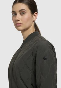 Gequilted bomberjack in donkergroen met een geribbelde kraag. Voorzien van een knoopsluiting en een subtiele logopatch op de linker mouw.