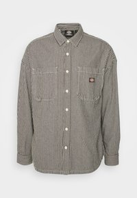 Camicia button-up con righe marroni e bianche, due taschini frontali e una piccola etichetta con logo sul petto. Presenta un colletto classico e chiusura con bottoni.