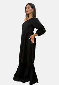 Abito maxi nero off-shoulder con maniche lunghe, dettagli in pizzo ai polsini e all'orlo, e una silhouette fluida. Tessuto liscio con una leggera lucentezza.