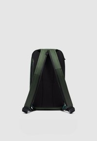 Mochila verde con respaldo de malla negra, correas acolchadas y cremalleras dobles. Textura suave con costuras reforzadas y herrajes ajustables.