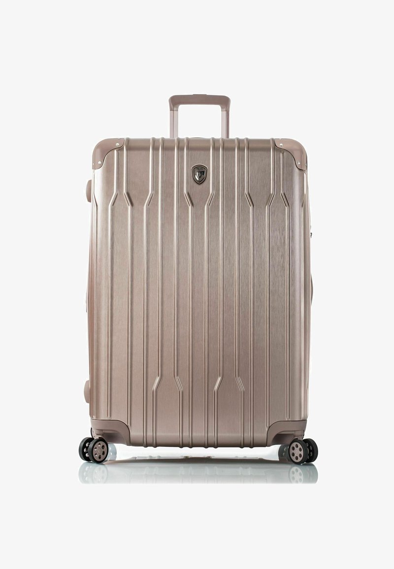 Valise rigide en rose gold métallique, avec des rainures verticales, une poignée télescopique et quatre roues pivotantes pour une maniabilité aisée.