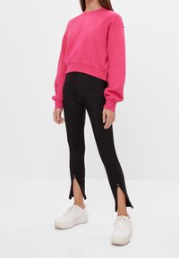 Felle roze cropped sweatshirt met oversized mouwen, gecombineerd met zwarte leggings met zijritsen en witte sneakers.